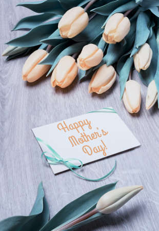 Greeting card "Happy Mother's Day".Orange tulips and a paper card on wooden table. This image is toned.の写真素材