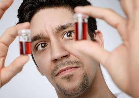 Young male medic or researcher holds up liquid samples. Shallow DOF, focus on the face. This image is toned.の写真素材