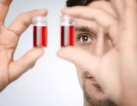 Young male medic or researcher holds up liquid samples. Shallow DOF, focus on the face. This image is toned.の写真素材