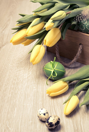 Easter composition with yellow tulips and Easter eggs on wooden table. This image is toned.