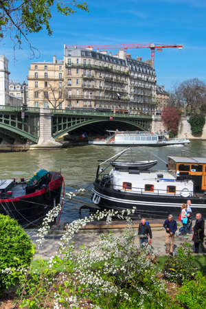 PARIS, FRANCE - APRIL 20 2016: Passenger boats pass Ile Saint-Louis, as people walk along the river through the gardens of Quai Saint Bernard.のeditorial素材