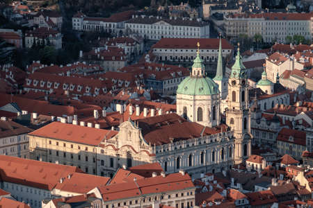 St. Nicolas church and roofs of Prague illuminated with the last rays of setting Sunの写真素材