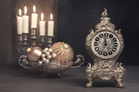 Vintage alarm clock showing five to twelve and burning candles in candlestick in a study room. Happy...