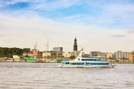 HAMBURG, GERMANY- AUGUST 12, 2015: Boat with tourists goes on Elbe river in Hamburg with St. Michael church spire visible.のeditorial素材