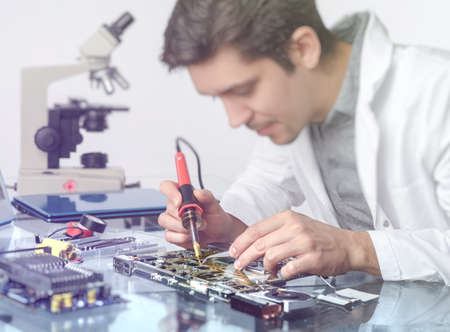 Electronics background. Young energetic male tech or engineer repairs electronic equipment in research facility. Shallow DOF, focus on the hands of the worker. This image is toned.の写真素材