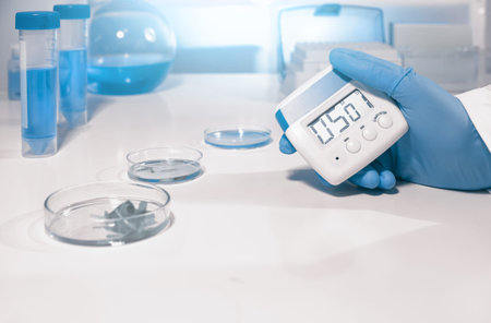 Scientific, medical or education background. Biological or biochemical lab out of focus, closeup on gloved hand holding digital timer. Focus on the hand.の写真素材