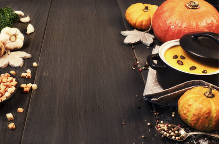 Pumpkin creme soup in a dark ceramic pan on the dark background. Ingredients: pumpkins, carrots, onions, garlic, parsley, salt and pepper, also croutons and pumpkin seeds for serving . Text space.の写真素材