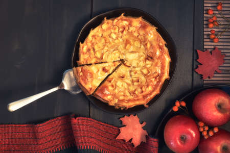 Homemade apple pie on dark plate with apples, red napkin and Autumn decorations on dark wooden background.  Top view, toned image.の写真素材