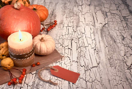Autumn still life with pumpkins, burning candle and paper tag on a rustic table. Text space, toned imageの写真素材