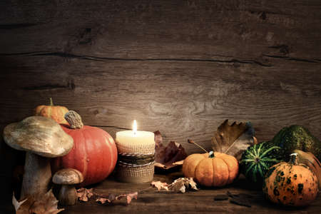 Autumn still life with burning candle, pumplins and seasonal decorations on wood. Space for your text on wooden background. This image is toned.の写真素材