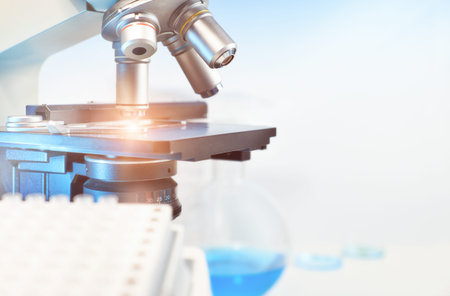 Scientific background with closeup on light microscope and laboratory out of focus. This image is...