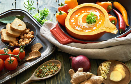 Spicy vegetable cream soup seasoned with chili, ginger and garlic. Served in a hollowed pumpkin with cream and parsley. Autumn food background, text space.の写真素材