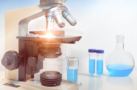 Scientific background with closeup on light microscope and laboratory out of focus. This image is...