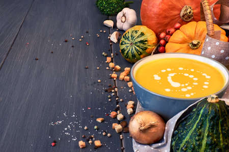 Pumpkin creme soup in grey ceramic bowl on the dark background. Ingredients: pumpkin, onions, parsley, salt and pepper, also croutons and pumpkin seeds for serving . Text space, toned image.の写真素材