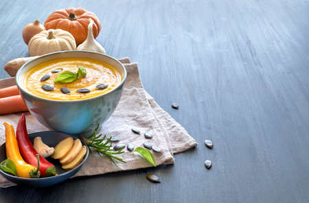 Spicy pumpkin soup with carrot, chili, ginger and garlic, served with basi and pumpkin seeds. Wooden background, text spaceの写真素材