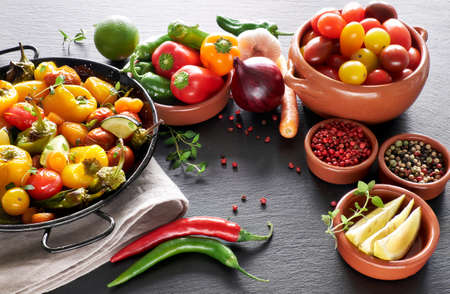 Rustic, oven baked vegetables with spices and herbs in baking dish. Seasonal vegetarian vegan meal on dark stone. Ingredients: zucchini, tomatoes, pepper, bell pepper, pumpkin, onion and garlic.の写真素材