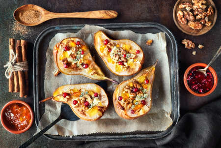 Pears baked with Blue cheese and wallnuts, served with orange and cowberry jam, cinnamon and sugar on dark background. Top viewの写真素材