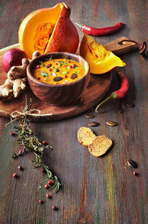 Spicy pumpkin soup in wooden bowl on dark background, served with pumpkin seeds and thyme leaves. Ingredients are around the bowl.の写真素材