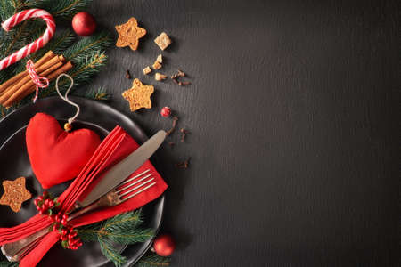Christmas menu concept on dark stone slate background. Black plates and vintage cutlery with Christmas decorations in green, red and orange. Space for your text on stone.の写真素材