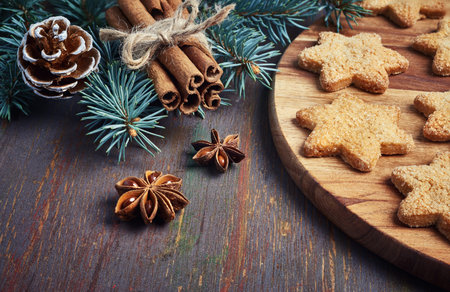 Christmas background with Christmas tree twigs, star-shaped cookies and spices on rustic wood. 