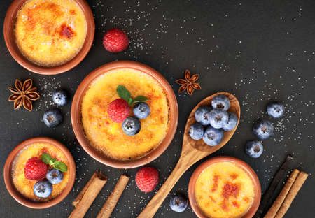 Creme brulee (cream brulee, burnt cream) with raspberry, blueberry and mint in terracota clay baking dishes. Top view, dark stone background.の写真素材