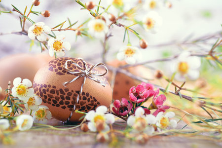Painted brown Easter egg on wood with white flowers and hay aroundの写真素材