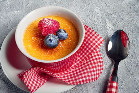 Creme brulee (cream brulee, burnt cream) with raspberry and blueberry, powdered with sugar on rough gray concrete backgroundの写真素材