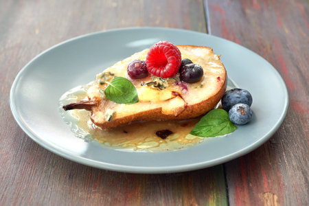 Closeup on half baked pear with blue cheese and sugar, served withraspberry, blueberry and mint leaves on gray plateの写真素材
