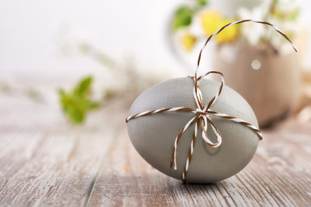 Closeup on grey Easter egg tied with checkered cord with flowers on wood, text space
