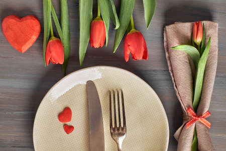Springtime menu concept with light yellow plate and cutlery decorated with fresh tulips on gray woodの写真素材