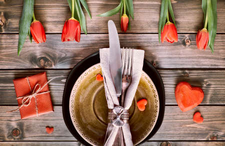 Springtime menu concept with light yellow plate and cutlery decorated with fresh tulips on rustic wooden tableの写真素材
