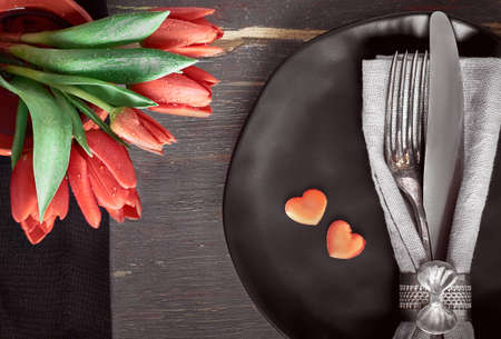 Springtime menu concept. Black plates, black napkins, vintage cutlery with red tulips and decorative hearts.の写真素材