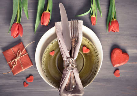 Springtime menu concept with light yellow plate and cutlery decorated with fresh tulips on rustic wooden tableの写真素材