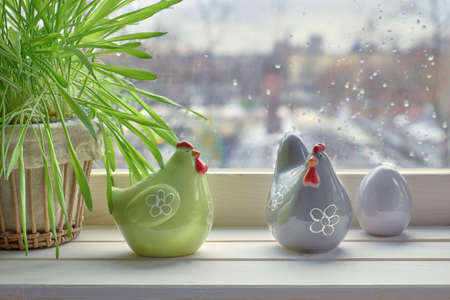Cat grass and two ceramic hens with egg near the window on a rainy day. This is early Springtime background with space for your text.の写真素材