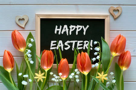 Easter composition with blackboard framed with spring flowers, tulips and lily of the valley. Text "Happy Easter" on the blackboard.の写真素材