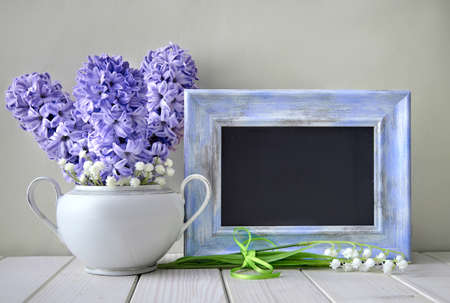 Blue springtime background. Blue hyacinth  and lily of the valley flowers around blackboard in blue frame. Space for your text on the board.の写真素材