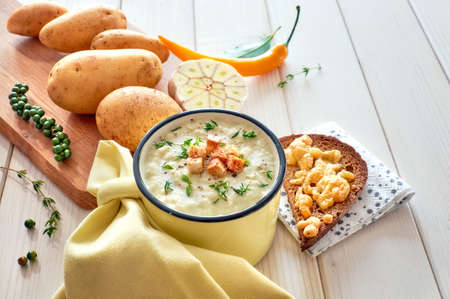 Homemade cream of potato soup with croutons, served with bread toasted with cheese on light wooden table. Spices: garlic, thyme, Prik Thai peppercorns, yellow chili, bay leaf.の写真素材