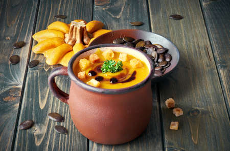 Tasty pumpkin soup in old enamel mug on rustic wooden table. The soup is served with croutons, parsley and pumpkin oil.の写真素材