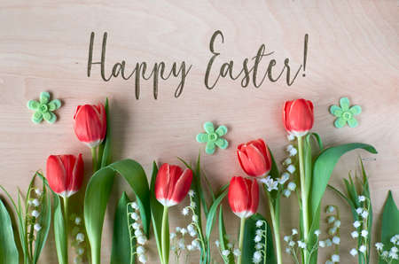 Easter composition with with spring flowers, tulips and lily of the valley on wood. Text "Happy Easter" embossed on the woodの写真素材