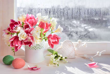 Pink tulips and white freesia flowers with Easter decorations on the window board, sunshine after rainの写真素材