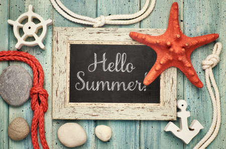 Blackboard with "Hello Summer!" chalk text, with sea shells, rope and star fish on light green wooden backgroundの写真素材