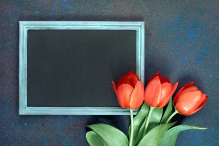 Blackboard and bunch of red tulips on abstract dark background, space for your test. Flat lay, toned image.の写真素材