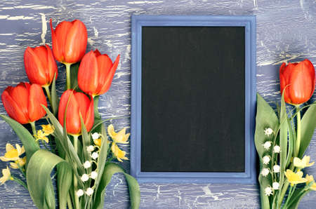 Blackboard and bunch of red tulips and lily of the valley flowers on rustic background. Space for your test, flat lay, toned image.の写真素材