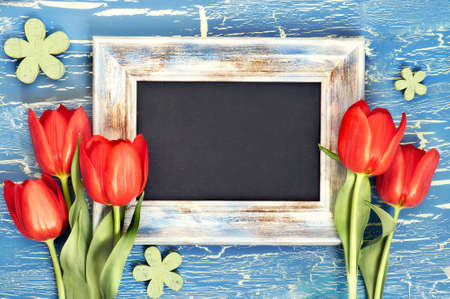 Blackboard and bunch of red tulips and lily of the valley flowers on blue rustic background. Space for your test, flat lay, toned image.の写真素材