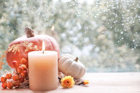Burning candle, Hokkaido pumpkin and Fall decorations on a window board on a rainy day, text spaceの写真素材