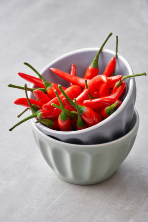 Closeup on red hot chili peppers in a stack of two grey ceramic bowls onr light gray background