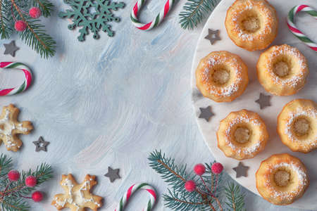 Mini bundt ring cakes with icing sugar on light background with fir twigs, berries and candy canes. Christmas holiday sweet food, flat lay with text space.の写真素材