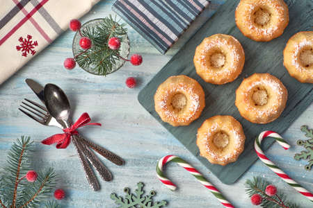 Mini bundt ring cakes with icing sugar on light background with fir twigs, berries and candy canes. Christmas holiday sweet food.の写真素材