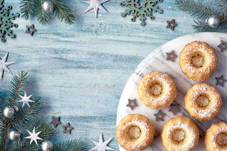 Mini bundt ring cakes with icing sugar on light background with fir twigs, berries and candy canes. Christmas holiday sweet food, flat lay with text space.の写真素材