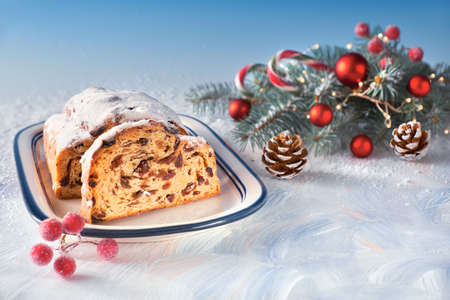 Christmas stollen on white-blue festive background with fir twigs and trinkets. Traditional German dessert for Christmas celebration, horizontal image with copy-space.の写真素材